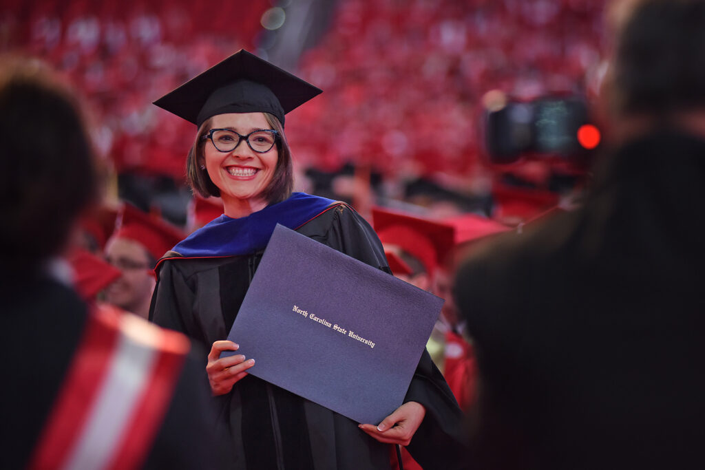Smiling doctoral student at graduation holding her diploma.